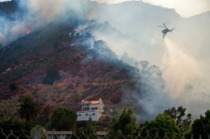 A helicopter drops water to protect a home from the Holy Fire in Lake Elsinore, California on Aug. 10, 2018.(Credit: ROBYN BECK/AFP/Getty Images)