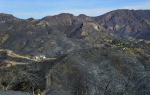 A house in the distance was left unscathed from the Woolsey Fire despite its fire-ravaged and charred mountainous surroundings as seen from a destroyed house on Lobo Canyon Road south of Agoura Hills on Nov. 15, 2018, one week after the deadly blaze started. (Credit: Frederic J. Brown / AFP / Getty Images)