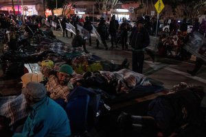 A group of Central American migrants moving toward the U.S. rest near El Chaparral port of entry at the U.S.-Mexico border after a demonstration as Federal Police guards walk by in Tijuana on Nov. 22, 2018. (Credit: Guillermo Arias / AFP / Getty Images)