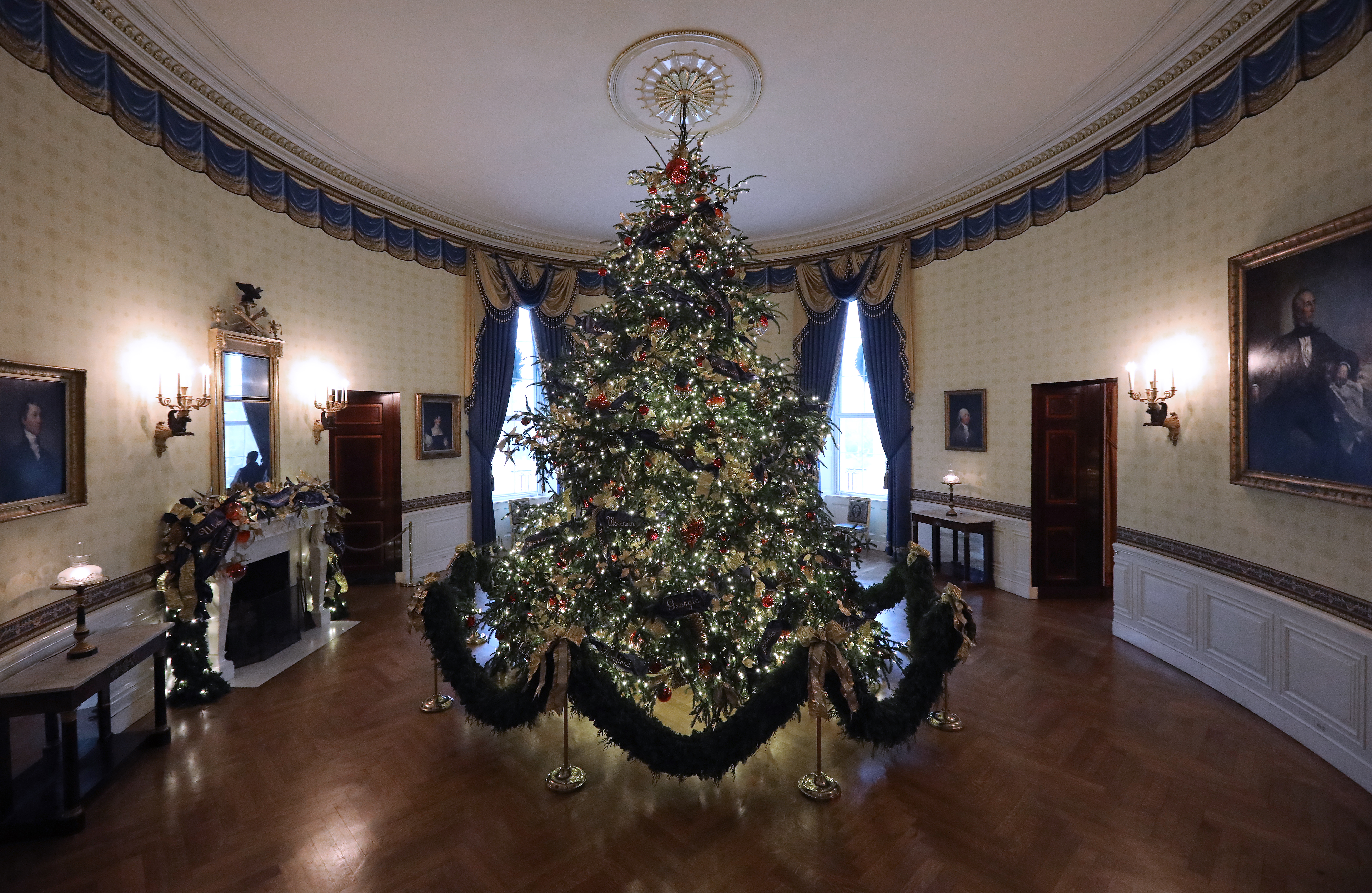 At 18 feet tall, the official White House Christmas is dressed in over 500 feet of blue velvet ribbon embroidered in gold with each state and territory, on display inside the Blue Room at the White House November 26, 2018 in Washington, DC. (Credit: Chip Somodevilla/Getty Images)