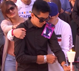 A photo of 3-year-old Nathan Luna, who was killed at his Fontana home on Nov. 1, 2018, sits on the shoulder of a man tearfully grieving the child's death during a vigil the following day. (Credit: RMG News)