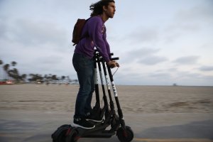A man rides a Bird shared dockless electric scooter while transporting three others along Venice Beach on Aug. 13, 2018, in Los Angeles. (Credit: Mario Tama/Getty Images)