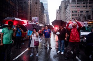 Onlookers take pictures on Seventh Avenue after a helicopter crash-landed on top of a building in midtown Manhattan in New York on June 10, 2019. (Credit: JOHANNES EISELE/AFP/Getty Images)
