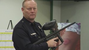 LAPD Lt. Jeff Bratcher holds a paintball gun during a news conference warning about their improper use on June 13, 2019. In the background, a victim's injury from a paintball gun in shown. (Credit: KTLA)