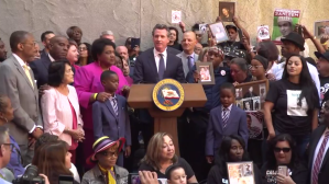 Gov. Gavin Newsom is surrounded by those who've lost family members to police shootings as he signs AB 392 on Aug. 19, 2019, in a still from a livestream shared by state Sen. Toni Atkins.