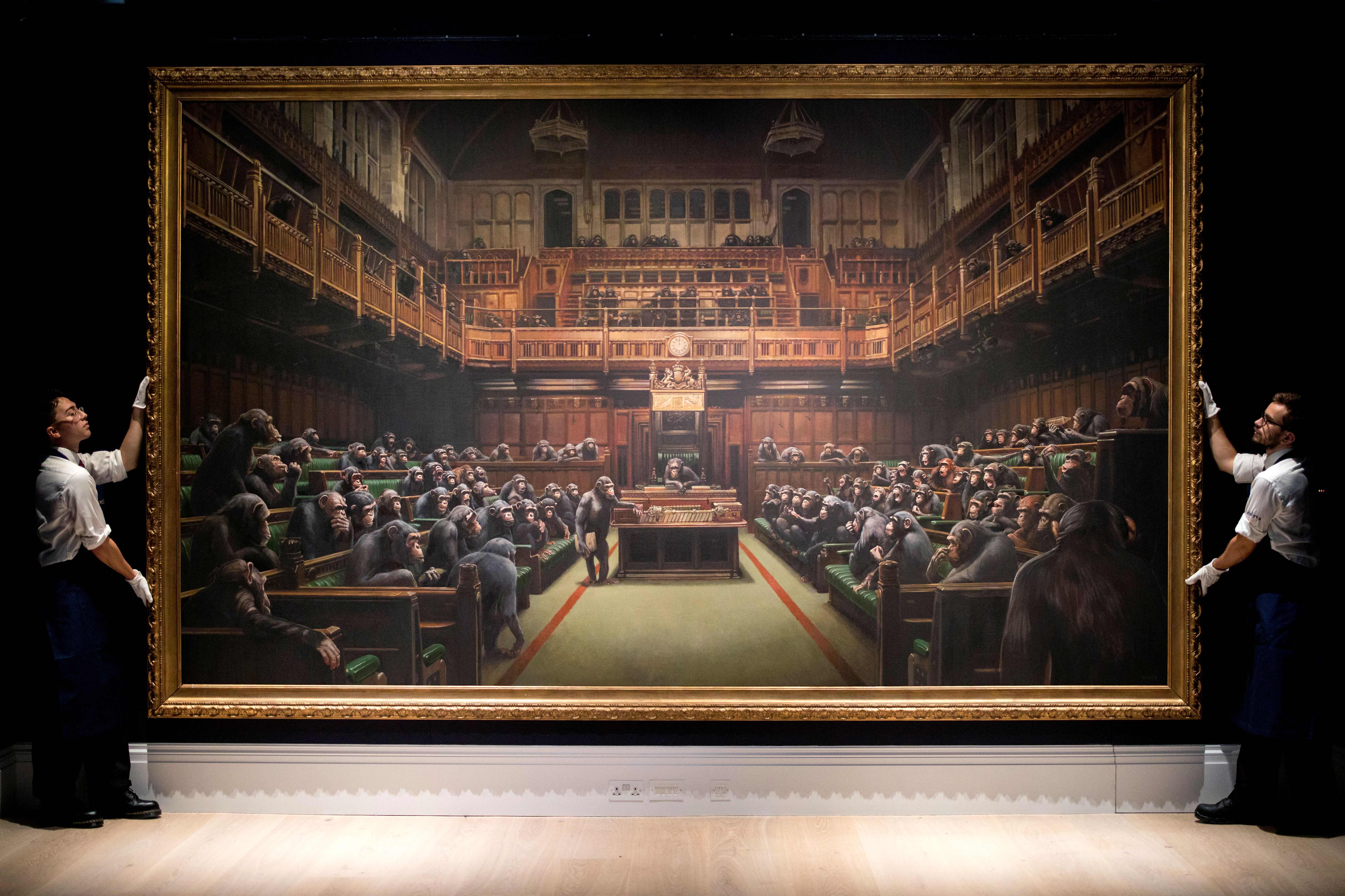 Gallery assistants pose with an artwork entitled 'Devolved Parliament' by British artist Banksy, during a press view in London on September 27, 2019. (Credit: TOLGA AKMEN/AFP/Getty Images)