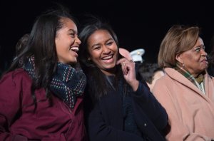 First daughters Malia (L) and Sasha (C) share a laugh on the Ellipse of the National Mall December 3, 2015 in Washington, DC. The First Family was joined by celebrities and guests to light the National Christmas tree during an evening of performances. AFP PHOTO / JIM WATSON / AFP / JIM WATSON (Photo credit should read JIM WATSON/AFP/Getty Images)