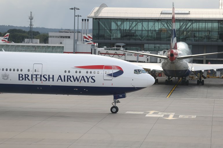 A British Airways 777 taxis near a terminal building.