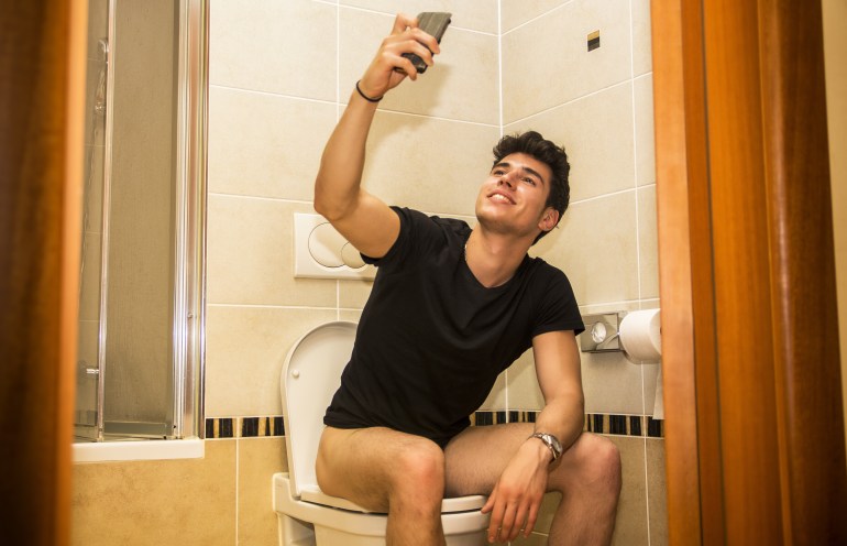 Smiling young man taking selfie while defecating