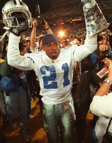 TEMPE, AZ - JANUARY 28: Dallas Cowboys cornerback Deion Sanders hoists the Vince Lombardi Super Bowl trophy as he walks off the field to the locker room after defeating the Pittsburgh Steelers 28 January during Super Bowl XXX at Sun Devil Stadium in Tempe, Arizona. The Cowboys won 27-17. (Photo credit should read VINCE BUCCI/AFP/Getty Images)
